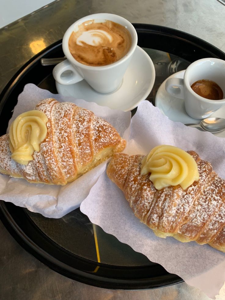 Due cornetti alla crema con cappuccino e caffè su un vassoio al tavolino